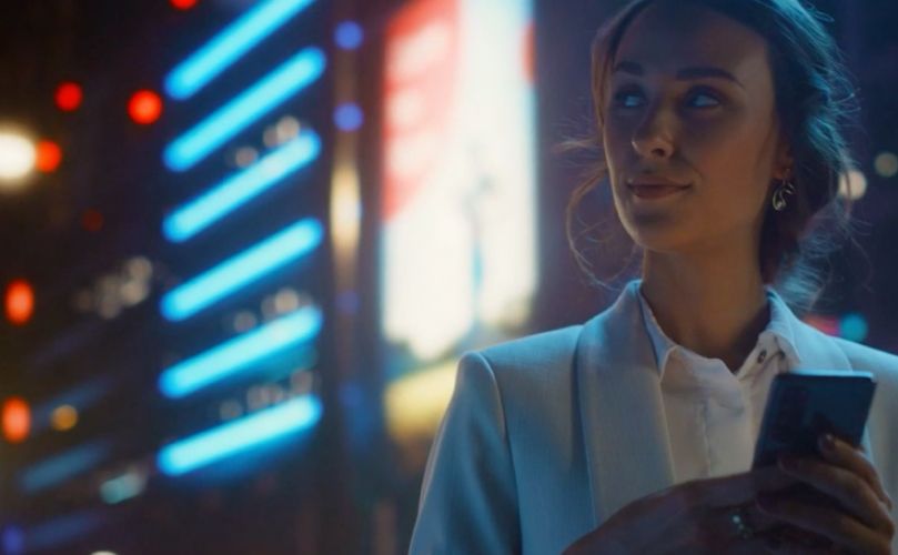 A woman looking to the side with a city full of lights as her background