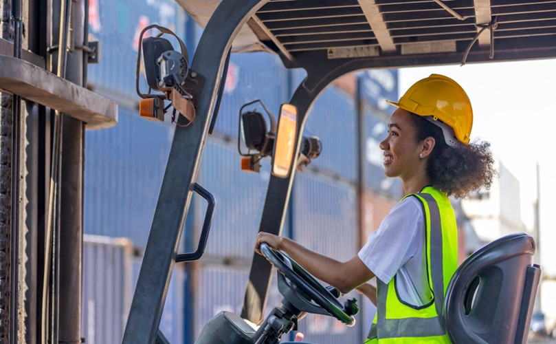 Smiling woman in helmet and safety vest driving a forklift.