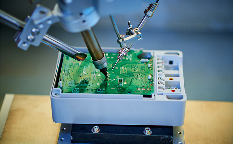 A robotic arm performing automated soldering on an electronic circuit board.