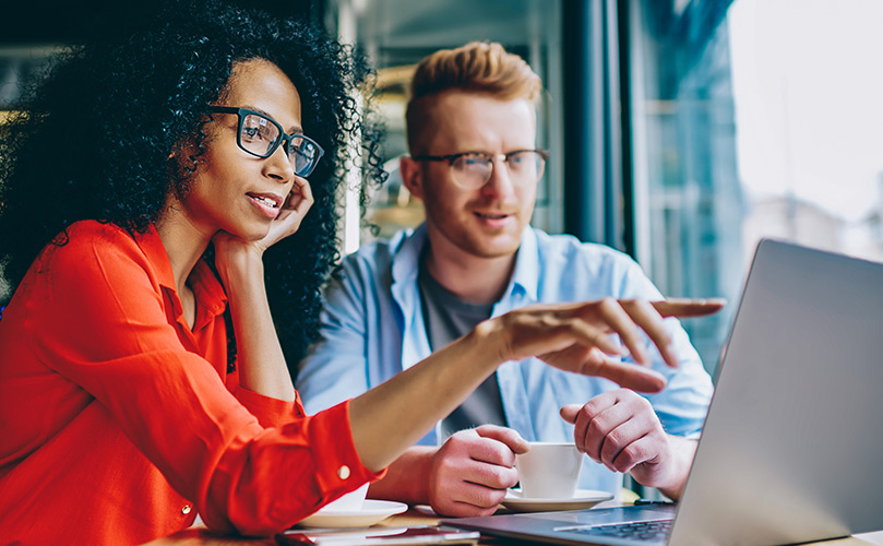 a woman and a man pointing at a screen while looking at a laptop