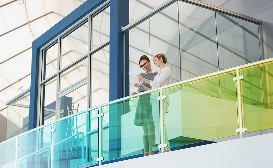 Two women review a tablet on a modern balcony.