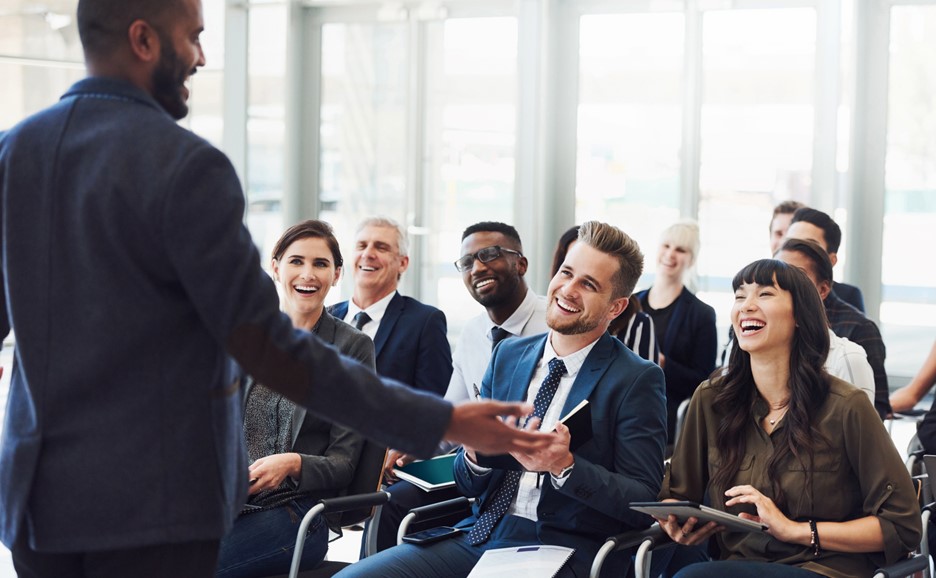 A speaker addressing a laughing audience at a conference or event.