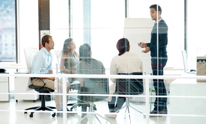 Several men and women having a meeting in a glass-walled conference room
