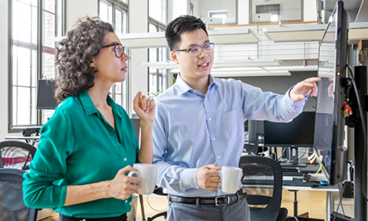 A business scene where two people (a man and a woman) are talking while pointing at a TV screen