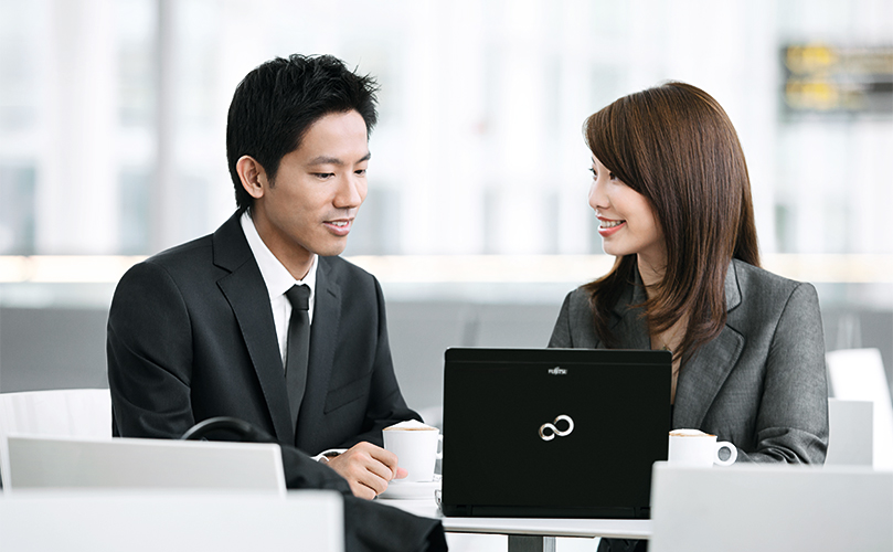 Two people discussing business while seated with a laptop in a café-like setting.